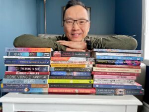Wayne Ng pictured with stacks of books written by his CanLit friends