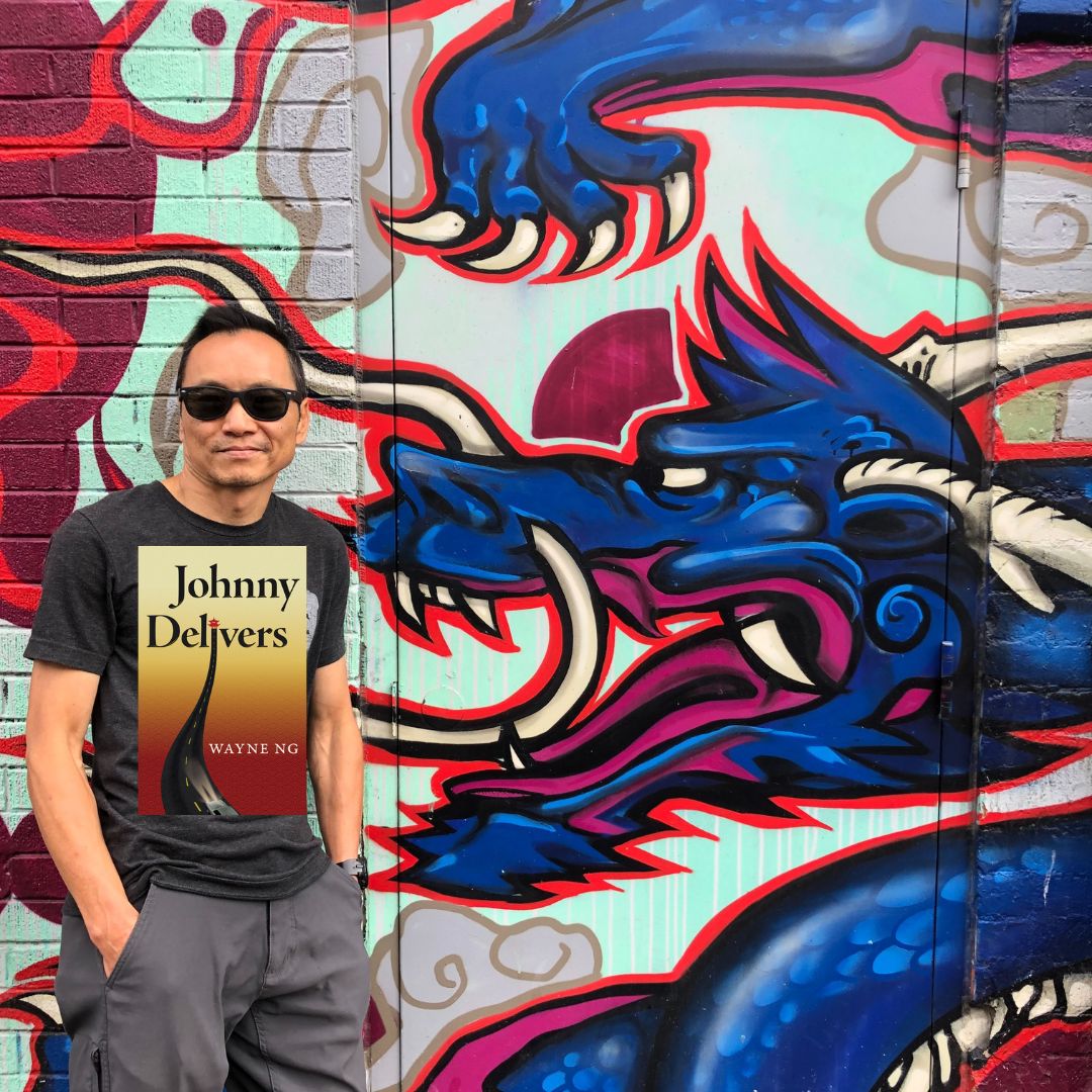 Photo of Wayne Ng with his book JOHNNY DELIVERS, in front of a wall with a Dragon on it in Kensington Market / Chinatown Toronto