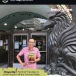 Wayne Ng is pictured holding a copy of JOHNNY DELIVERS before the Lillian H. Smith Branch of the Toronto Public Library on College St, Toronto